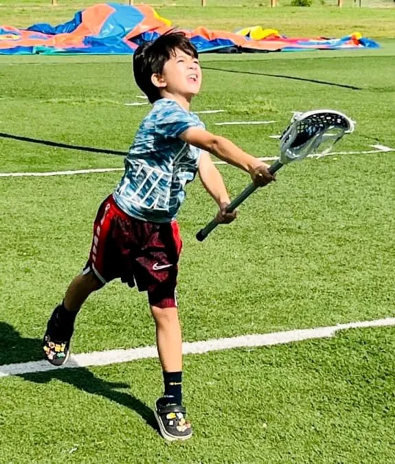 A camper carrying a lacrosse stick down the field