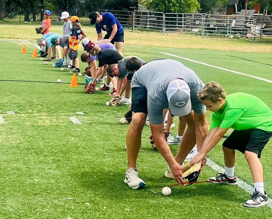 A Revo Sports coach teaching fielding technique to young players on the grass