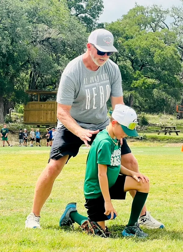 A coach kneeling beside a player to talk through a drill